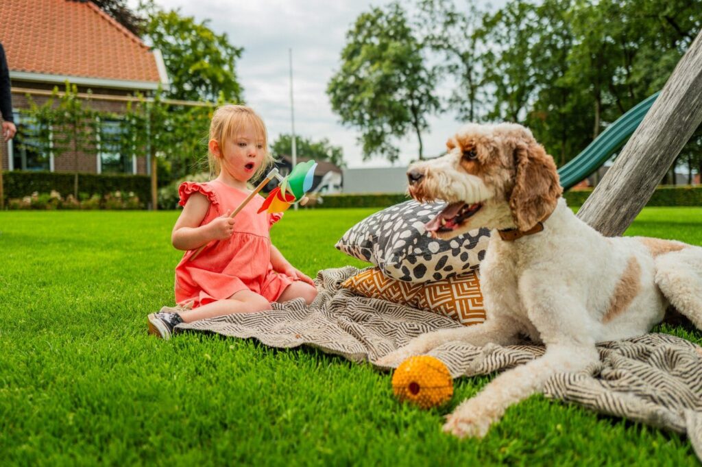 Kind met windmolentje zit naast hond op het gras in de tuin