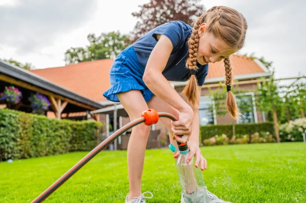 Kind bevestigt waterslang aan plastic fles op graszoden