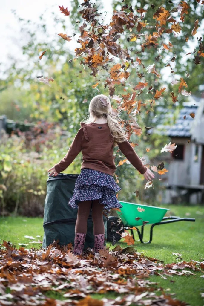 Kind gooit bladeren in de lucht op een gazon