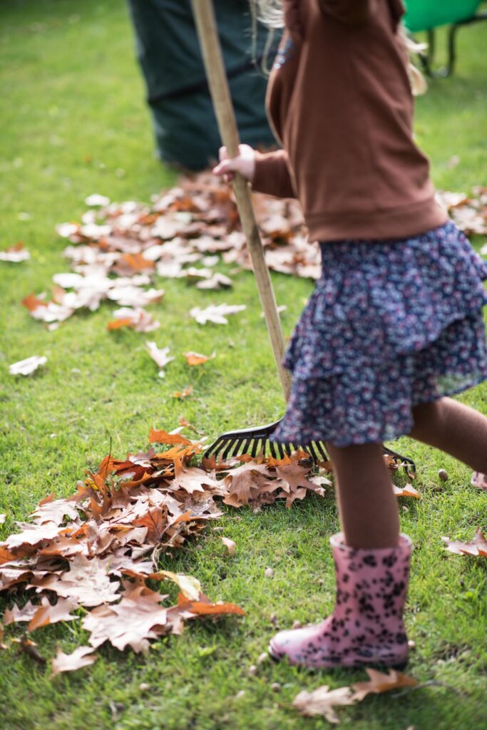 Meisje harkt bladeren op grasveld in de tuin