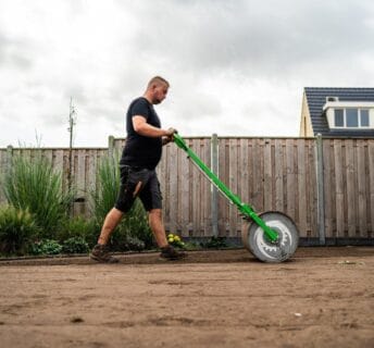 Hovenier walst geëgaliseerde zandgrond aan als voorbereiding op het leggen van graszoden