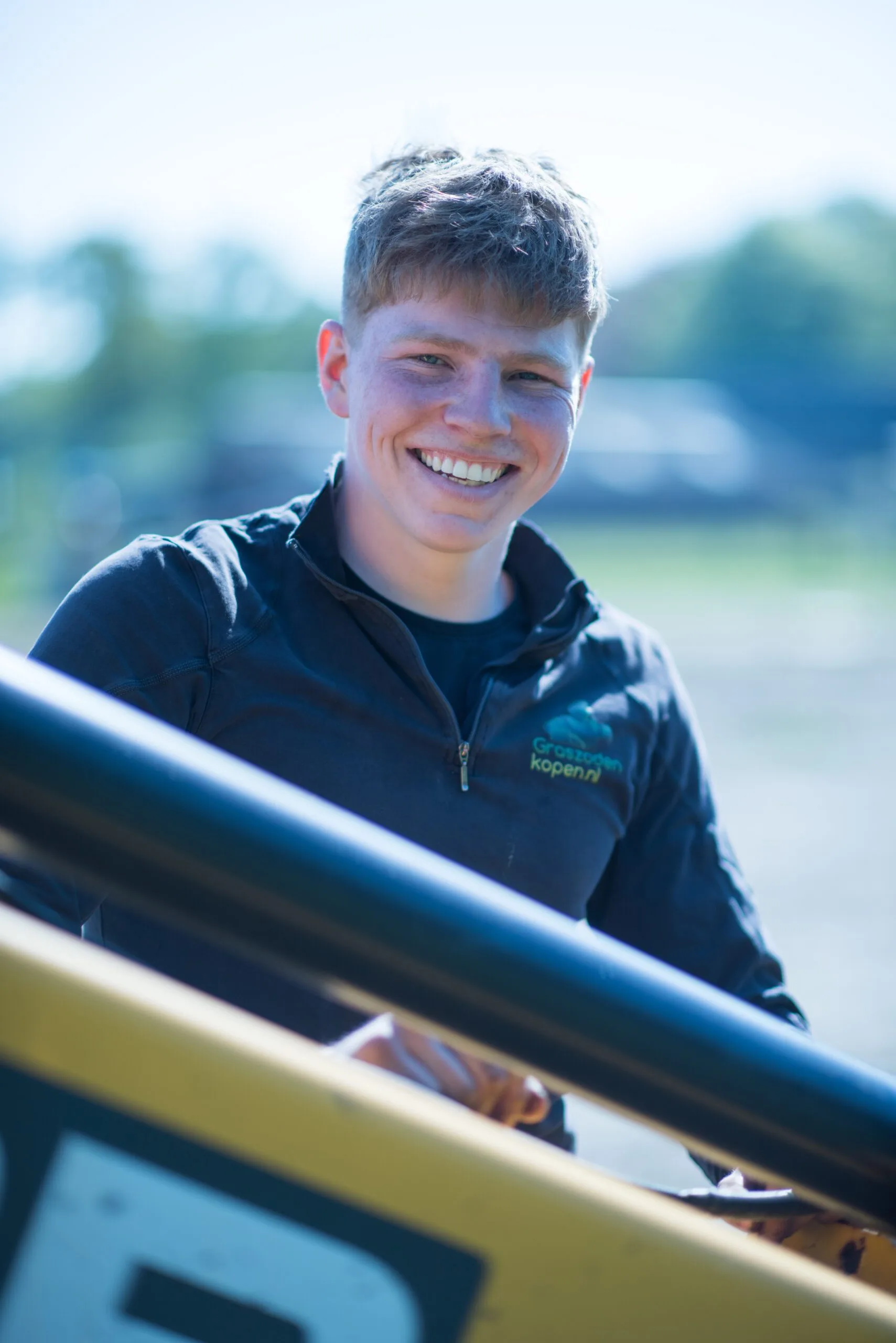 Jonge medewerker van Graszodenkopen.nl lachend bij de shovel op het veld
