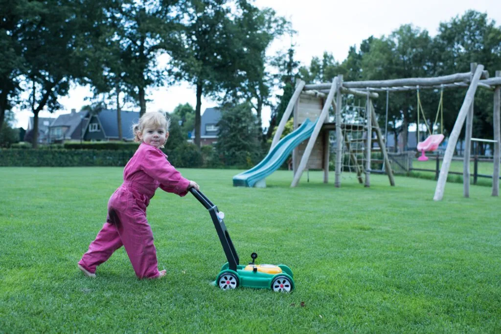 Kind dat met een speelgoedgrasmaaier over een strak groen gazon loopt, symbool voor een veilig en speelklaar grasveld.