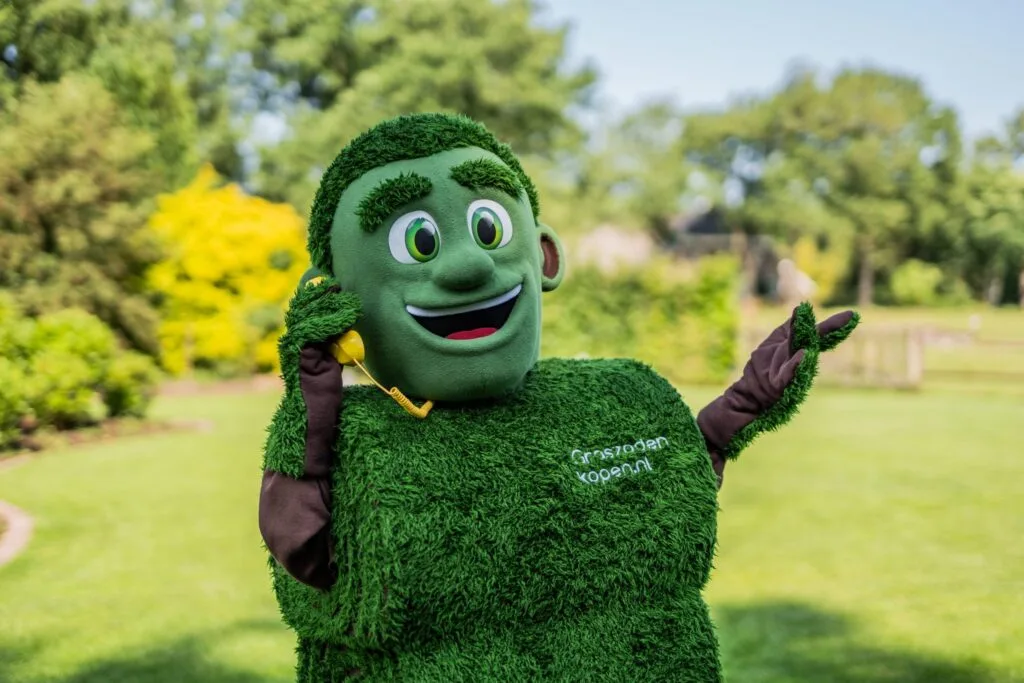 Grasmattie van Graszodenkopen.nl belt vrolijk met een gele telefoon in een groene tuin