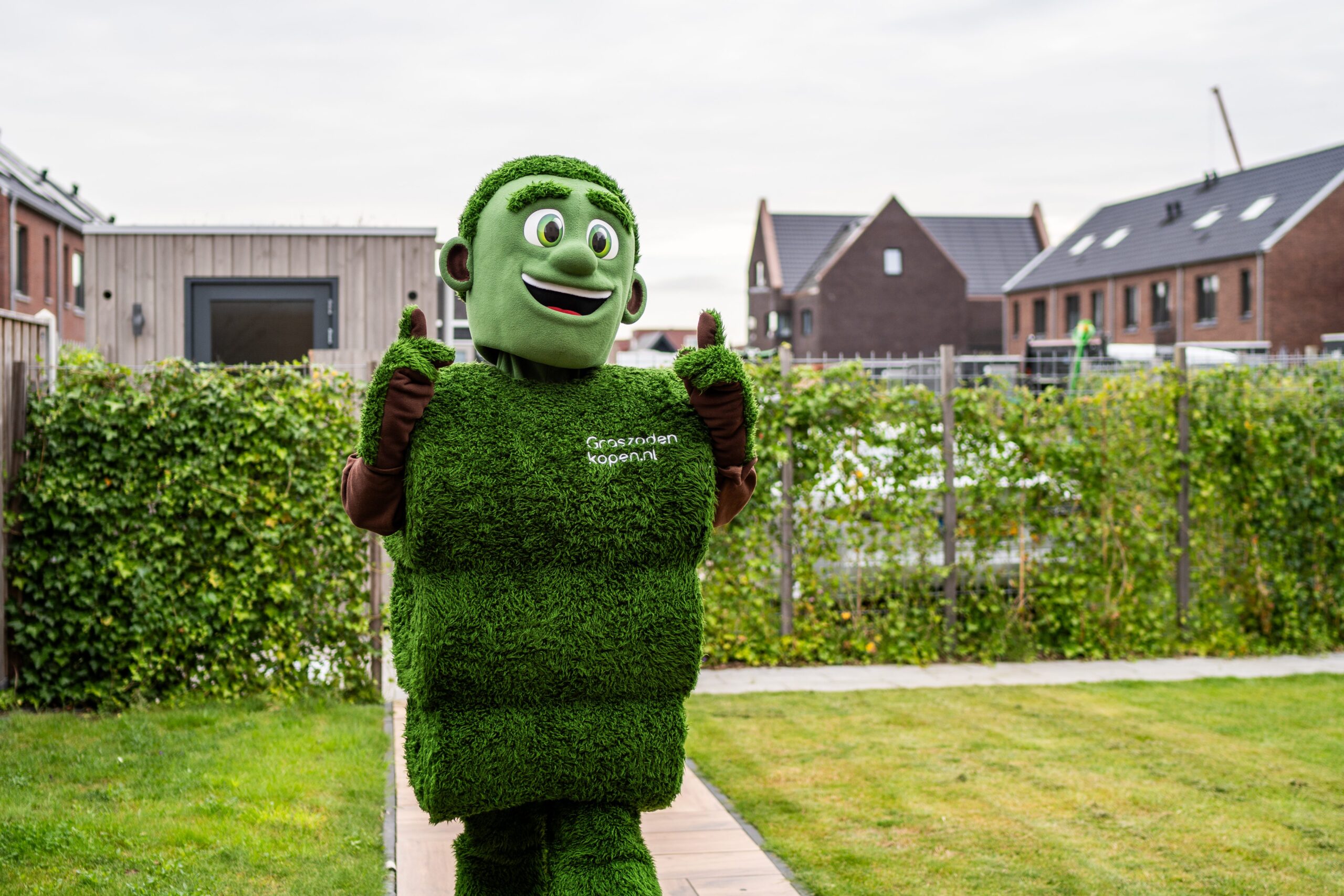 Grasmattie, de mascotte van Graszodenkopen.nl, in een tuin met een vrolijke duim omhoog