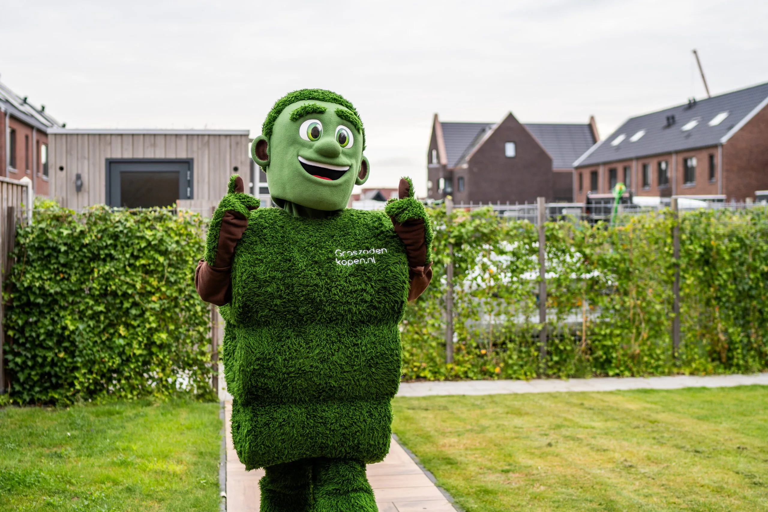 Grasmattie, de mascotte van Graszodenkopen.nl, in een tuin met een vrolijke duim omhoog