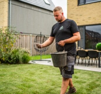 Hovenier strooit zand over graszoden met een zwarte emmer