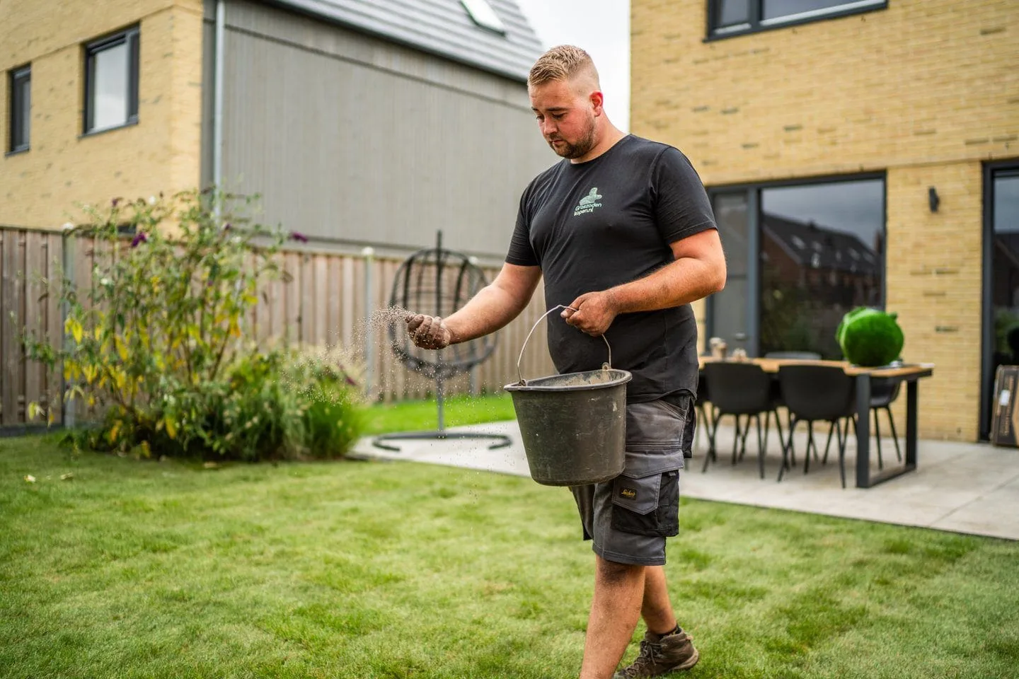 Hovenier strooit zand over graszoden met een zwarte emmer