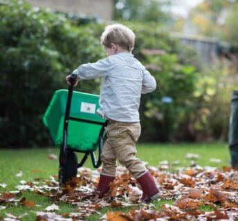 Jongen met rode laarzen en kruiwagen op gras met bladeren