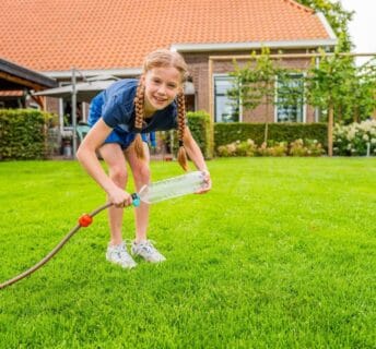 Kind test sproeier van fles en slang op graszoden