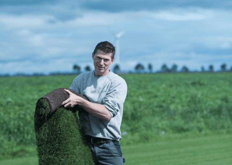 Medewerker van een graszodenbedrijf houdt een rol graszoden vast op het veld