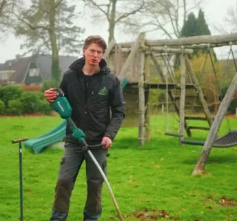 Medewerker bewerkt het gazon naast een houten schommel in een achtertuin